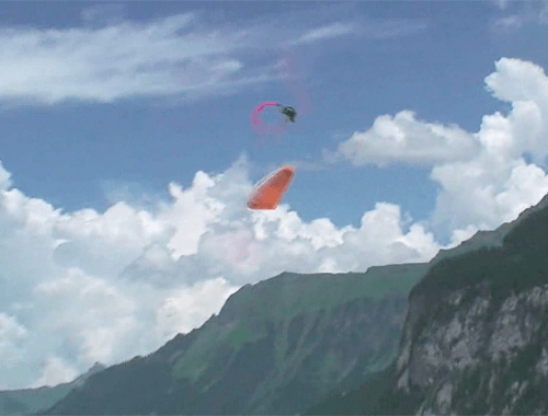 Parapente laranja realiza um Infinity Tumbling com montanhas ao fundo